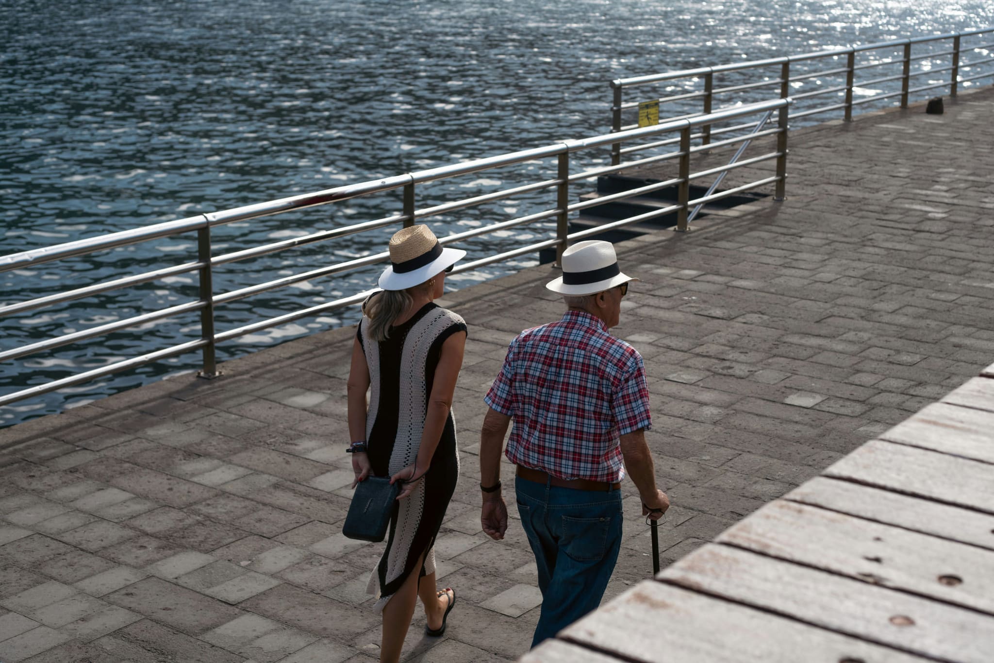 Symbolbild: Ein älteres Paar spaziert an einer Uferpromenade, von hinten gesehen.