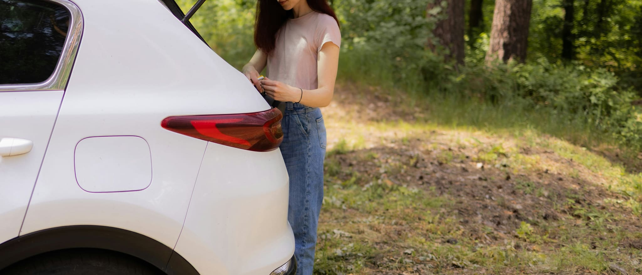 Symbolbild: Eine junge Frau öffnet die Heckklappe eines Autos am Waldrand.