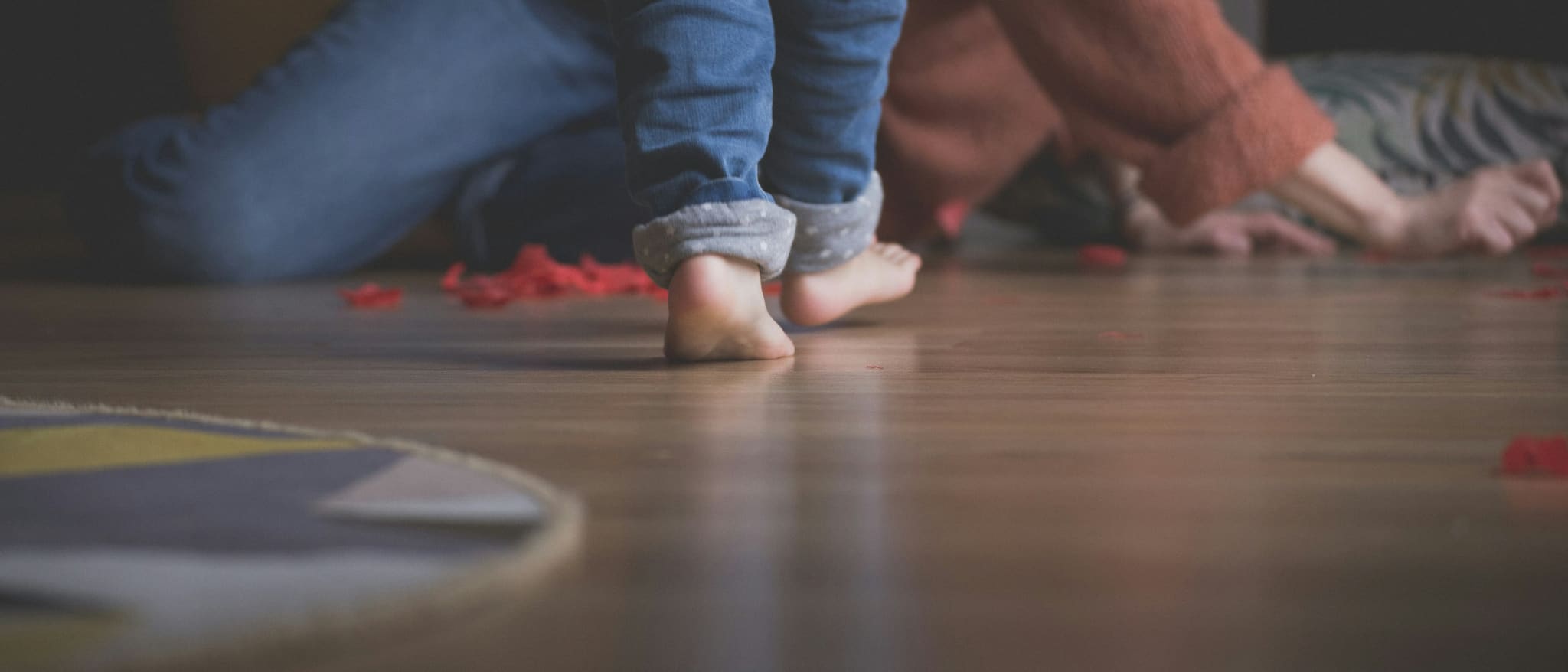 Symbolbild: Kinderfüße und ein Erwachsener beim Spielen auf dem Holzboden im Wohnzimmer.