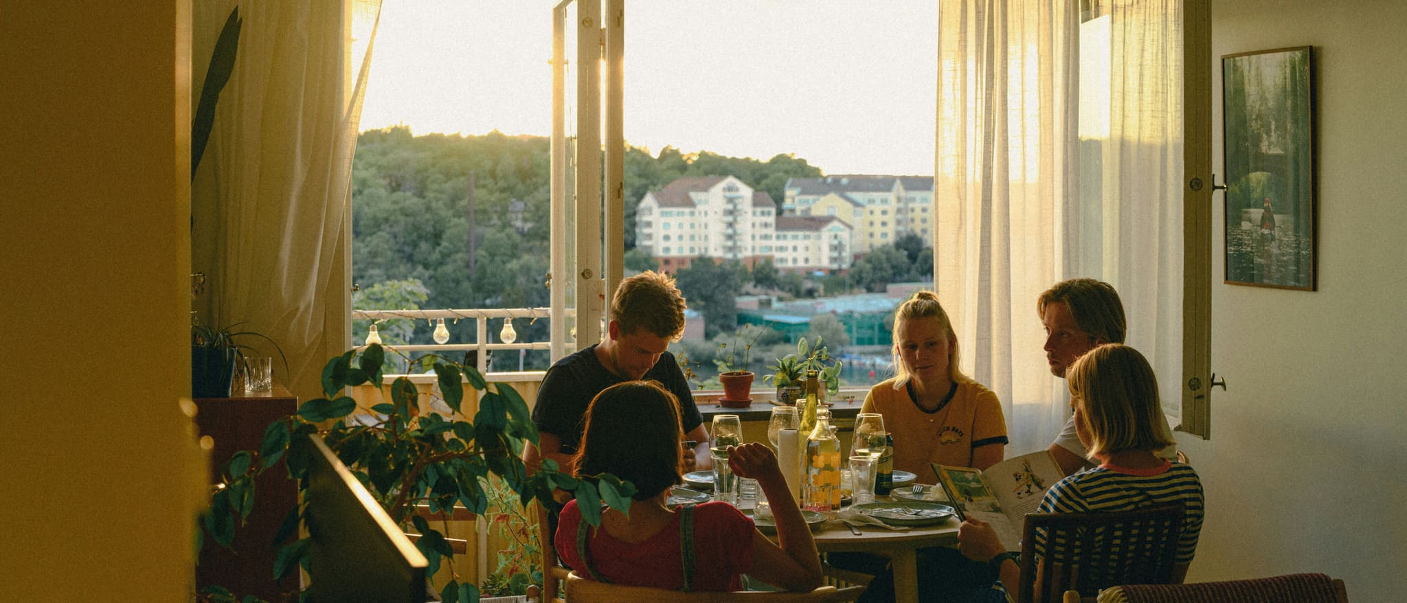 Symbolbild: Mehrere Menschen sitzen am Abend an einem Esstisch vor einem offenen Fenster.